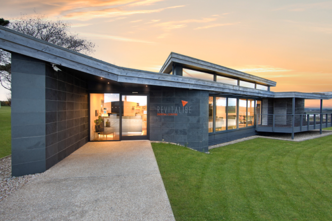 revitalisedentalcentre_header_image - Revitalise Dental Centre | Private Dentist Cornwall Modern dental clinic exterior at sunset with a glass entrance and dark stone walls.