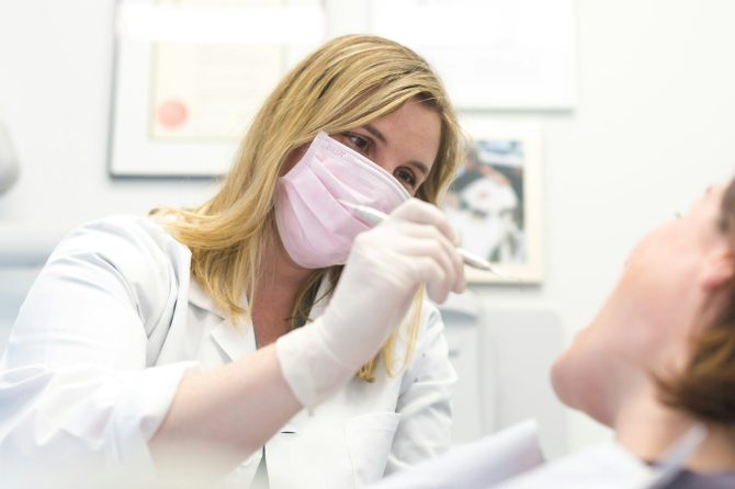 anish-kumar-d3ksDplsnGk-unsplash - Revitalise Dental Centre | Private Dentist Cornwall Dentist in a white coat wearing a pink mask examines a patient with dental instruments in a clinic
