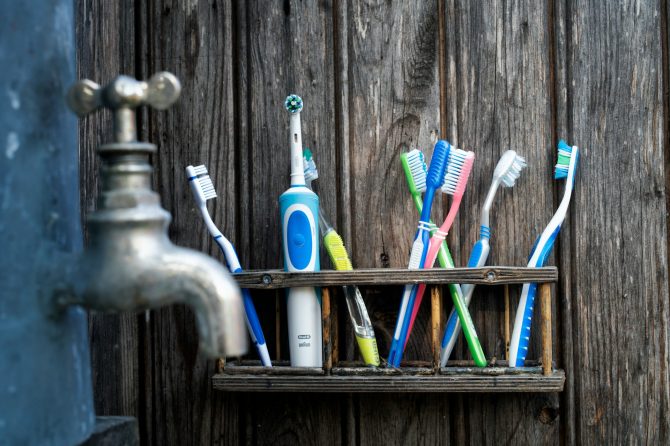 Colorful toothbrushes in a rustic wooden holder against a weathered wood backdrop.